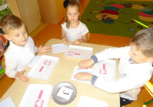 Trójka dzieci siedzi przy stole, na tackach mają ułożoną mapę i godło Polski.